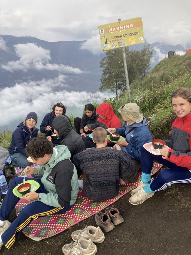 Trekkers enjoying dinner at Senaru Crater Rim campsite with breathtaking sunset views of Mount Rinjani’s crater and Segara Anak Lake in Lombok, Indonesia.