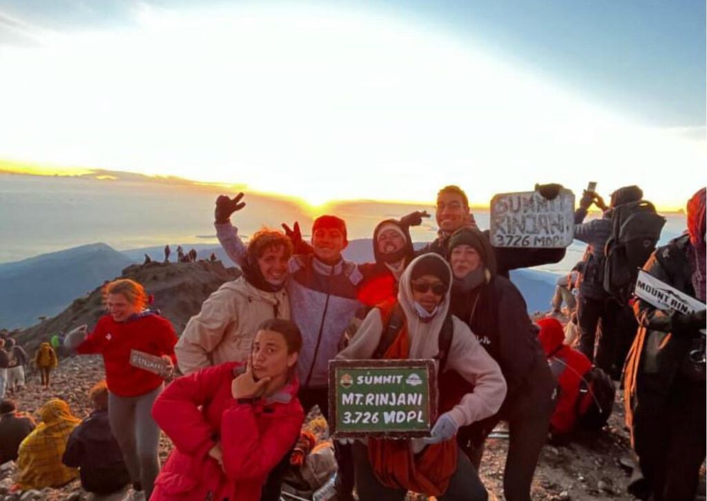 Sunrise view from Mount Rinjani summit with hikers overlooking Lombok island and volcanic landscape