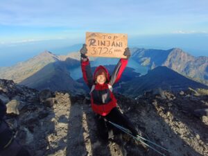 Hikers standing at the summit of Mount Rinjani during sunrise with panoramic views of volcanic landscapes, clouds, and the crater lake below.