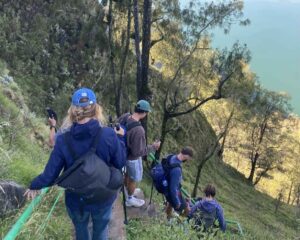 Trekkers descending steep trails from Senaru Crater Rim campsite toward Segara Anak Lake on Mount Rinjani surrounded by dramatic volcanic landscapes and green mountain scenery.